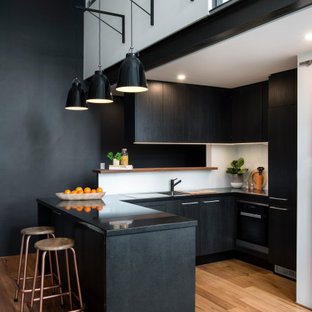 Design ideas for a contemporary u-shaped kitchen in Sydney with an undermount sink, flat-panel cabinets, black cabinets, white splashback, panelled appliances, medium hardwood floors, a peninsula, brown floor and black benchtop.