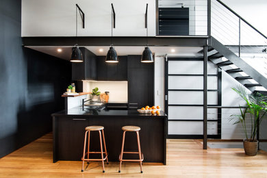 This is an example of a small urban u-shaped kitchen/diner in Sydney with a built-in sink, white splashback, glass sheet splashback, black appliances, medium hardwood flooring, a breakfast bar and black worktops.