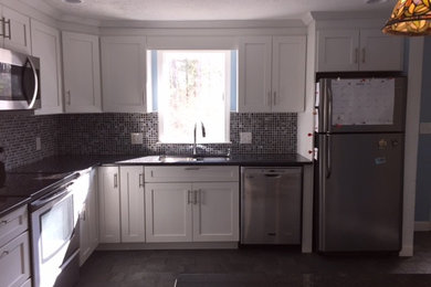 Example of a mid-sized transitional l-shaped porcelain tile enclosed kitchen design in Boston with an undermount sink, shaker cabinets, white cabinets, granite countertops, black backsplash, glass tile backsplash, stainless steel appliances and an island