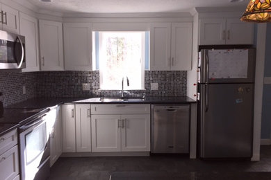 Imagen de cocinas en L tradicional renovada de tamaño medio cerrada con fregadero bajoencimera, armarios estilo shaker, puertas de armario blancas, encimera de granito, salpicadero negro, salpicadero de azulejos de vidrio, electrodomésticos de acero inoxidable, suelo de baldosas de porcelana y una isla