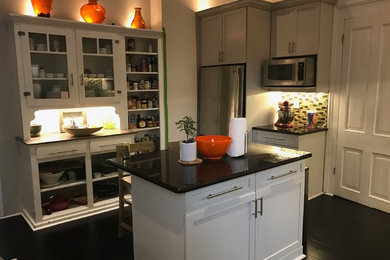 Bild på ett avskilt, stort vintage l-kök, med en undermonterad diskho, skåp i shakerstil, grå skåp, granitbänkskiva, grönt stänkskydd, stänkskydd i glaskakel, rostfria vitvaror, mörkt trägolv, en köksö och svart golv