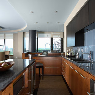 Ejemplo de cocina comedor en L, contemporánea, con armarios con paneles lisos, puertas de armario de madera oscura, salpicadero azul, fregadero bajoencimera, salpicadero de azulejos de vidrio, electrodomésticos de acero inoxidable, suelo de madera oscura, una isla y encimera de granito