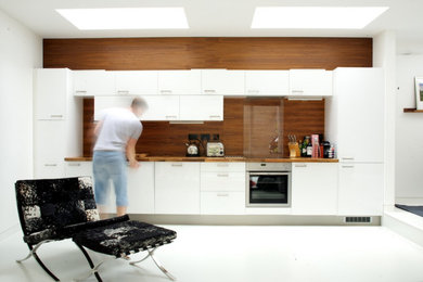 Medium sized contemporary single-wall kitchen/diner in London with a submerged sink, flat-panel cabinets, white cabinets, wood worktops, brown splashback, wood splashback, stainless steel appliances, concrete flooring, no island, grey floors and brown worktops.