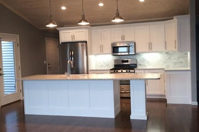 Mid-sized elegant l-shaped dark wood floor kitchen photo in Grand Rapids with an undermount sink, shaker cabinets, white cabinets, solid surface countertops, white backsplash, ceramic backsplash, stainless steel appliances and an island