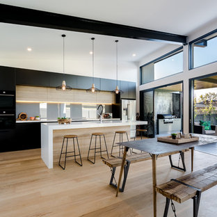 Design ideas for a large contemporary galley eat-in kitchen in Adelaide with flat-panel cabinets, glass sheet splashback, light hardwood floors, multiple islands, an undermount sink, black cabinets, grey splashback, beige floor and white benchtop.