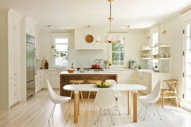 Klassisk inredning av ett vit vitt u-kök, med en rustik diskho, skåp i shakerstil, vita skåp, vitt stänkskydd, stänkskydd i sten, rostfria vitvaror, ljust trägolv, en köksö och beiget golv