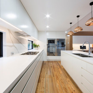 Photo of a large contemporary l-shaped eat-in kitchen in Canberra - Queanbeyan with flat-panel cabinets, white cabinets, white splashback, stainless steel appliances, with island, brown floor, an undermount sink, window splashback and medium hardwood floors.
