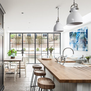 Ejemplo de cocina comedor de galera, nórdica, grande, con fregadero sobremueble, armarios con paneles empotrados, encimera de madera, electrodomésticos de acero inoxidable, una isla, puertas de armario negras, salpicadero blanco y suelo gris