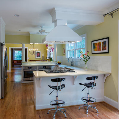 Mid-sized elegant u-shaped medium tone wood floor and brown floor open concept kitchen photo in Atlanta with a farmhouse sink, shaker cabinets, white cabinets, white backsplash, subway tile backsplash, stainless steel appliances and a peninsula
