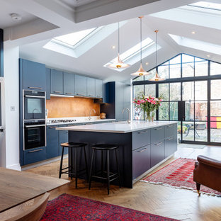 Esempio di una grande cucina contemporanea con ante lisce, lavello sottopiano, ante blu, paraspruzzi arancione, elettrodomestici in acciaio inossidabile, pavimento marrone e top bianco