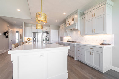 Example of a large farmhouse galley light wood floor and gray floor open concept kitchen design in Salt Lake City with an undermount sink, flat-panel cabinets, gray cabinets, quartz countertops, multicolored backsplash, marble backsplash, stainless steel appliances, an island and white countertops