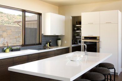 Photo of a large contemporary u-shaped enclosed kitchen in Salt Lake City with a submerged sink, flat-panel cabinets, white cabinets, composite countertops, grey splashback, metro tiled splashback, integrated appliances, dark hardwood flooring and an island.