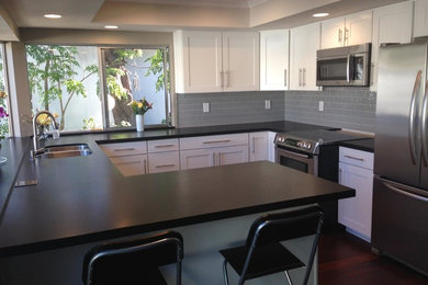 Example of a small trendy u-shaped medium tone wood floor kitchen design in Orange County with an undermount sink, shaker cabinets, white cabinets, granite countertops, gray backsplash, glass tile backsplash and stainless steel appliances