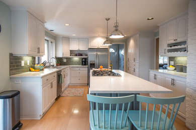 This is an example of a medium sized classic u-shaped kitchen in Seattle with a submerged sink, raised-panel cabinets, white cabinets, engineered stone countertops, grey splashback, glass tiled splashback, stainless steel appliances, light hardwood flooring and an island.