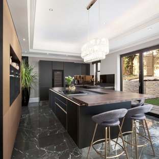 This is an example of an expansive contemporary u-shaped kitchen in Miami with an undermount sink, flat-panel cabinets, black cabinets, wood benchtops, panelled appliances, porcelain floors, with island, black floor and brown benchtop.