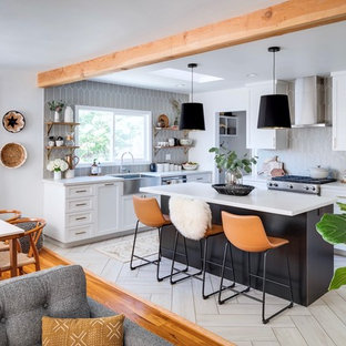 This is an example of a mid-sized transitional l-shaped eat-in kitchen in San Diego with a farmhouse sink, shaker cabinets, black cabinets, quartz benchtops, grey splashback, ceramic splashback, stainless steel appliances, porcelain floors, with island and white benchtop.