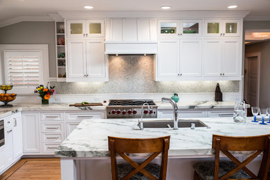 Klassisk inredning av ett kök, med en undermonterad diskho, luckor med infälld panel, vita skåp, marmorbänkskiva, mellanmörkt trägolv och en köksö