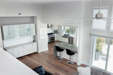 Example of a mid-sized trendy l-shaped vinyl floor and brown floor eat-in kitchen design in San Diego with a farmhouse sink, shaker cabinets, white cabinets, granite countertops, white backsplash, porcelain backsplash, stainless steel appliances, an island and gray countertops