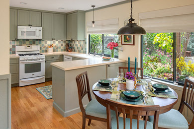 Example of a mid-sized arts and crafts u-shaped light wood floor and brown floor eat-in kitchen design in San Diego with shaker cabinets, blue cabinets, quartz countertops, multicolored backsplash, ceramic backsplash, white appliances, a peninsula and beige countertops