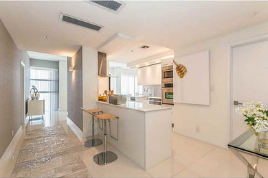 Inspiration for a mid-sized modern galley porcelain tile and white floor enclosed kitchen remodel in Miami with flat-panel cabinets, white cabinets, solid surface countertops, a peninsula, an undermount sink, multicolored backsplash, mosaic tile backsplash and stainless steel appliances