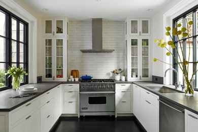 Design ideas for a traditional u-shaped enclosed kitchen in Philadelphia with a submerged sink, glass-front cabinets, white cabinets, white splashback, metro tiled splashback, stainless steel appliances and black floors.