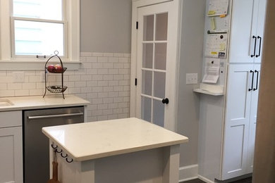 Inspiration for a small transitional u-shaped vinyl floor kitchen remodel in Milwaukee with a single-bowl sink, flat-panel cabinets, white cabinets, quartz countertops, white backsplash, ceramic backsplash, stainless steel appliances and an island
