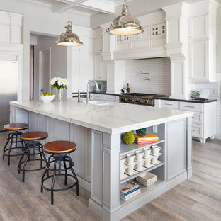 Idées déco pour une grand cuisine ouverte classique en L avec un évier encastré, un placard avec porte à panneau encastré, des portes de placard blanches, un plan de travail en quartz modifié, une crédence blanche, une crédence en carreau de céramique, un électroménager en acier inoxydable, un sol en carrelage de céramique, un îlot central et un sol marron.