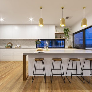 Photo of a mid-sized contemporary l-shaped kitchen in Canberra - Queanbeyan with ceramic splashback, medium hardwood floors, an undermount sink, flat-panel cabinets, white cabinets, grey splashback, black appliances, brown floor and grey benchtop.