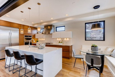 Photo of a medium sized contemporary l-shaped kitchen in Denver with a submerged sink, flat-panel cabinets, medium wood cabinets, engineered stone countertops, stainless steel appliances, light hardwood flooring, an island, white worktops and white splashback.