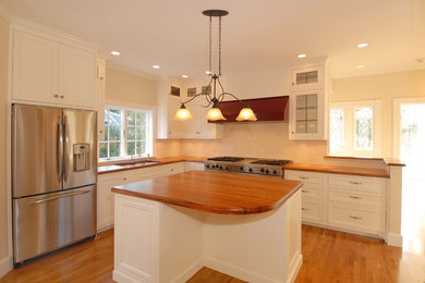 Example of a large classic l-shaped medium tone wood floor eat-in kitchen design in Boston with white cabinets, wood countertops, ceramic backsplash, stainless steel appliances, an island, a double-bowl sink and white backsplash