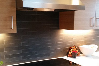 Idée de décoration pour une cuisine minimaliste en bois brun de taille moyenne avec un placard à porte plane, un plan de travail en surface solide, une crédence noire, une crédence en ardoise, un électroménager en acier inoxydable et un plan de travail blanc.