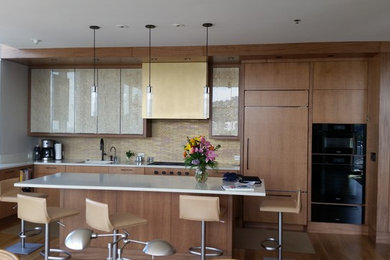Example of a mid-sized minimalist l-shaped medium tone wood floor and brown floor kitchen design in Portland with an undermount sink, flat-panel cabinets, medium tone wood cabinets, solid surface countertops, an island, white countertops, beige backsplash, glass tile backsplash and paneled appliances