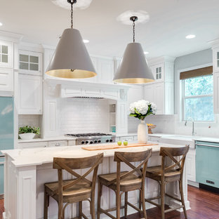 Transitional l-shaped medium tone wood floor and brown floor kitchen photo in Philadelphia with a farmhouse sink, raised-panel cabinets, white cabinets, white backsplash, subway tile backsplash, colored appliances and an island