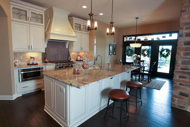 Eat-in kitchen - mid-sized transitional single-wall dark wood floor and brown floor eat-in kitchen idea in Phoenix with an undermount sink, raised-panel cabinets, white cabinets, granite countertops, beige backsplash, stone tile backsplash, stainless steel appliances and an island