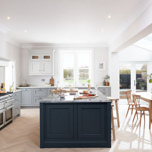This is an example of a large classic l-shaped kitchen/diner in London with shaker cabinets, grey cabinets, white splashback, light hardwood flooring, an island, stainless steel appliances, white worktops and beige floors.