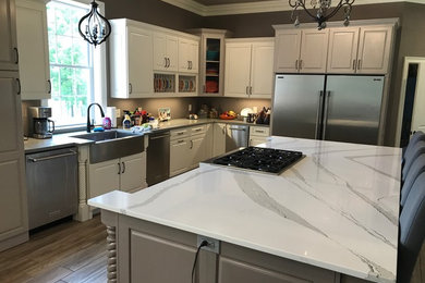 Inspiration for a mid-sized shabby-chic style l-shaped medium tone wood floor and brown floor kitchen remodel in Atlanta with a farmhouse sink, raised-panel cabinets, white cabinets, stainless steel appliances, an island and quartzite countertops