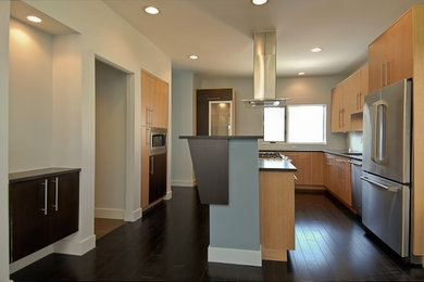 Cette image montre une cuisine américaine minimaliste en U et bois clair de taille moyenne avec un évier posé, un placard à porte plane, un électroménager en acier inoxydable, parquet foncé et une péninsule.