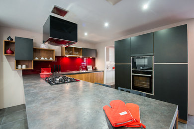 This is an example of a contemporary l-shaped open plan kitchen in London with a double-bowl sink, flat-panel cabinets, black cabinets, laminate countertops, red splashback, glass sheet splashback and black appliances.