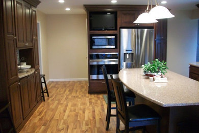 Photo of a traditional kitchen/diner in Chicago with recessed-panel cabinets, dark wood cabinets, stainless steel appliances, light hardwood flooring and an island.