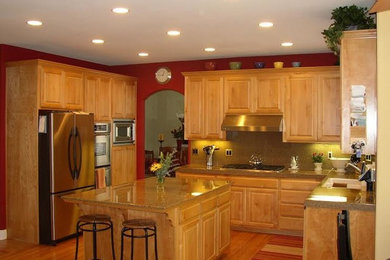 Klassisk inredning av ett avskilt, stort u-kök, med en dubbel diskho, luckor med upphöjd panel, skåp i mellenmörkt trä, granitbänkskiva, gult stänkskydd, rostfria vitvaror, ljust trägolv, en köksö och blått golv