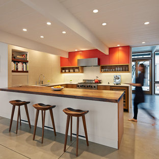 Mid-century modern kitchen ideas - Mid-century modern u-shaped concrete floor kitchen photo in San Francisco with flat-panel cabinets, orange cabinets, wood countertops and stainless steel appliances