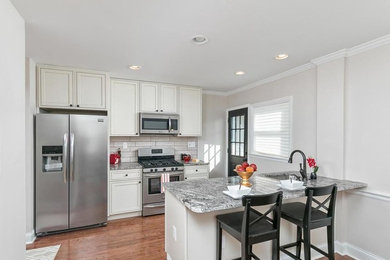 Example of a small classic brown floor eat-in kitchen design in Baltimore with a single-bowl sink, shaker cabinets, white cabinets, granite countertops, beige backsplash, ceramic backsplash, stainless steel appliances, an island and multicolored countertops