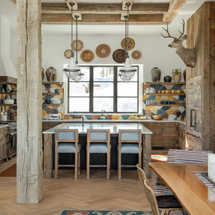 Modelo de cocina comedor en U, rústica, con puertas de armario con efecto envejecido, salpicadero multicolor, suelo de madera clara, una isla y encimeras blancas