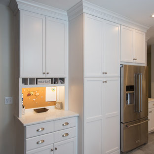 Inspiration for a mid-sized beach style u-shaped kitchen in Boston with a farmhouse sink, recessed-panel cabinets, white cabinets, quartz benchtops, grey splashback, stone tile splashback, stainless steel appliances, ceramic floors, a peninsula and grey floor.