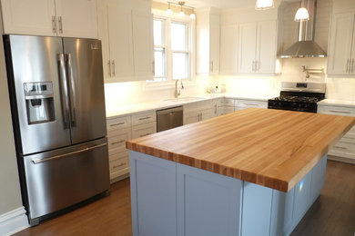 Example of a large trendy l-shaped medium tone wood floor eat-in kitchen design in Toronto with an undermount sink, shaker cabinets, white cabinets, quartzite countertops, white backsplash, subway tile backsplash, stainless steel appliances and an island