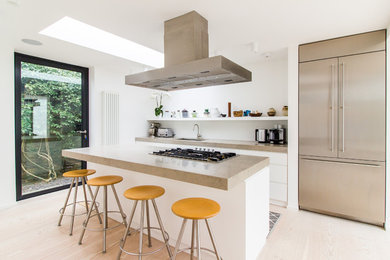 This is an example of a medium sized contemporary kitchen in London with an island, a submerged sink, flat-panel cabinets, white cabinets, light hardwood flooring, stainless steel appliances and beige floors.