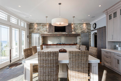 Example of a large beach style single-wall slate floor eat-in kitchen design in Philadelphia with a farmhouse sink, recessed-panel cabinets, gray cabinets, marble countertops, gray backsplash, glass tile backsplash, stainless steel appliances and an island