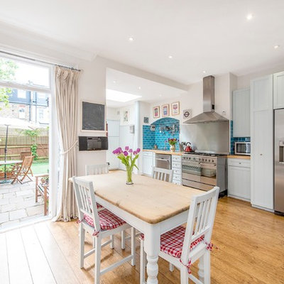 Elegant medium tone wood floor eat-in kitchen photo in London with shaker cabinets, white cabinets, wood countertops, blue backsplash, subway tile backsplash and stainless steel appliances
