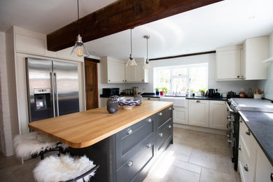 Design ideas for a traditional u-shaped kitchen/diner in Buckinghamshire with a belfast sink, shaker cabinets, blue cabinets, wood worktops, black appliances, limestone flooring, an island, beige floors and beige worktops.