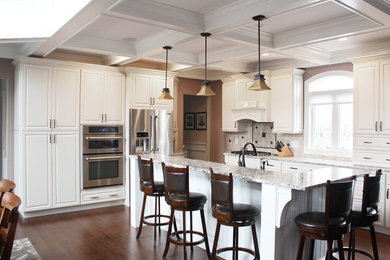 Inspiration for a mid-sized timeless l-shaped dark wood floor and brown floor eat-in kitchen remodel in New York with a drop-in sink, raised-panel cabinets, white cabinets, granite countertops, beige backsplash, travertine backsplash, stainless steel appliances, an island and multicolored countertops